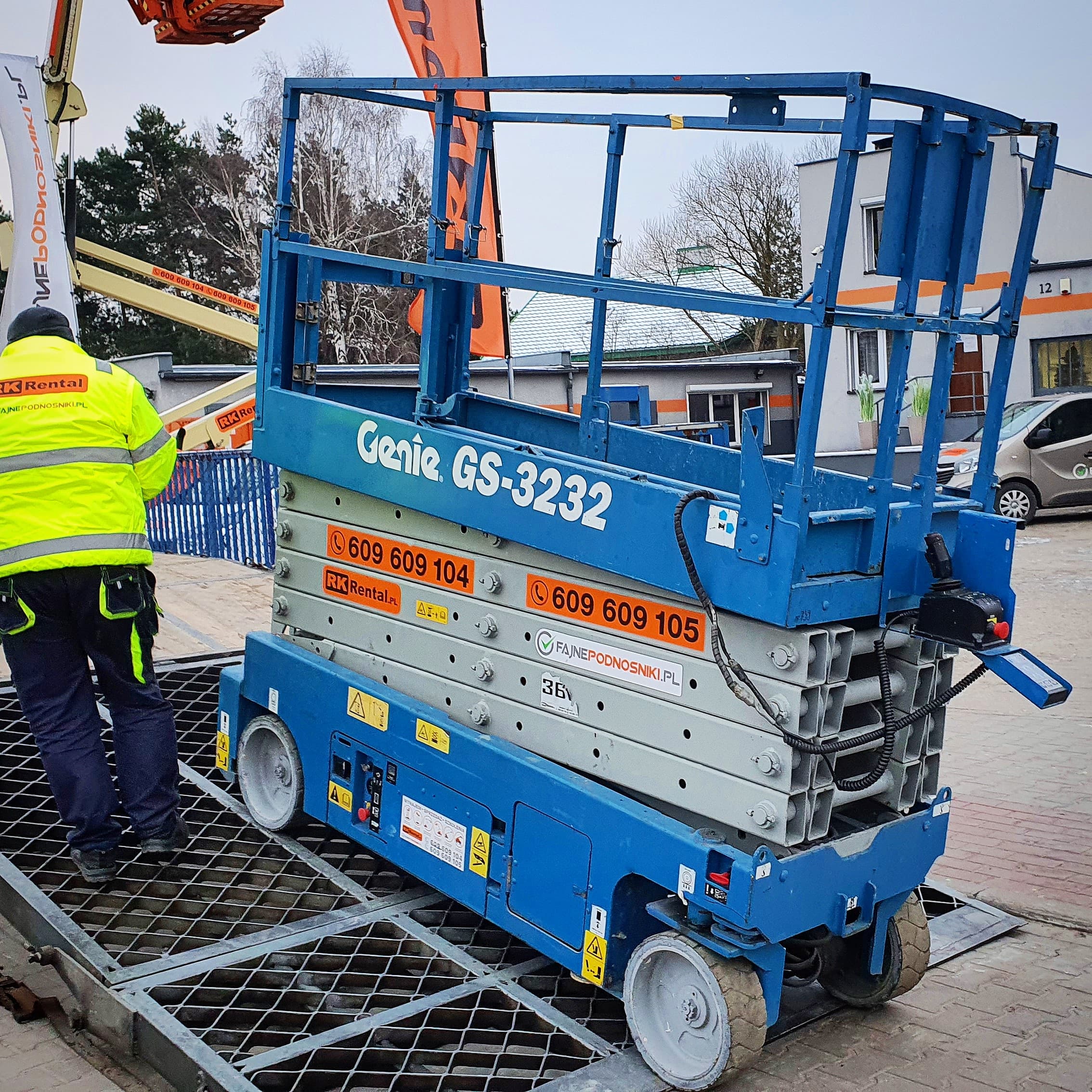 Podnośnik nożycowy elektryczny Genie GS-3232 RK Rental podczas rozładunku dźwigiem w Grudziądzu
