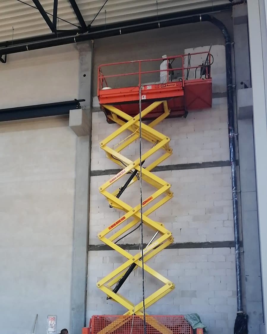 Podnośnik nożycowy elektryczny JLG M4069 na podporach RK Rental podczas prac na dużej wysokości w hali we Włocławku