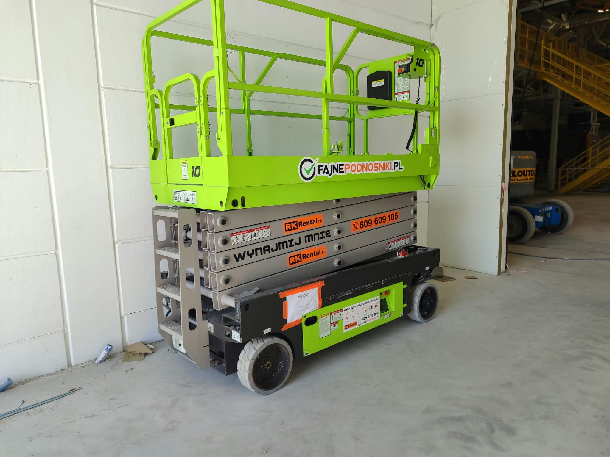 Podnośnik nożycowy elektryczny Zoomlion ZS1012AC Li (12 m) RK Rental w budowanej hali w Brodnicy przy ścianie z płyt warstwowych