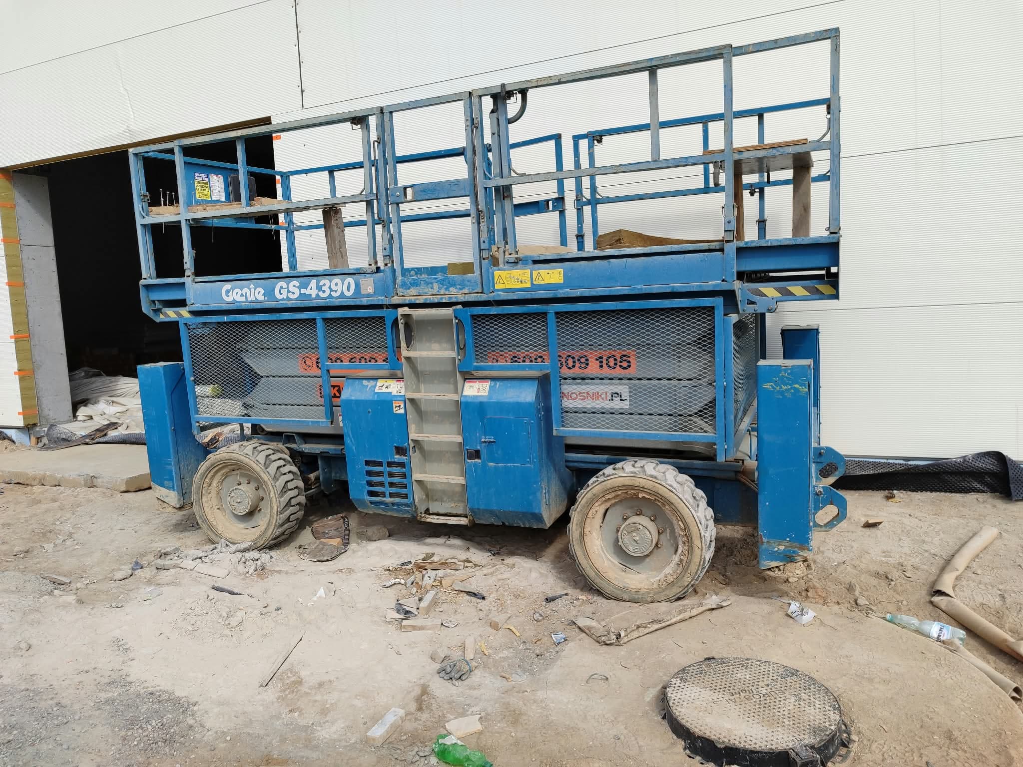 Terenowy podnośnik nożycowy Genie GS-4390 RT 4x4 RK Rental (15 m) przy bramie hali podczas montażu ścian z płyt warstwowych w Toruniu