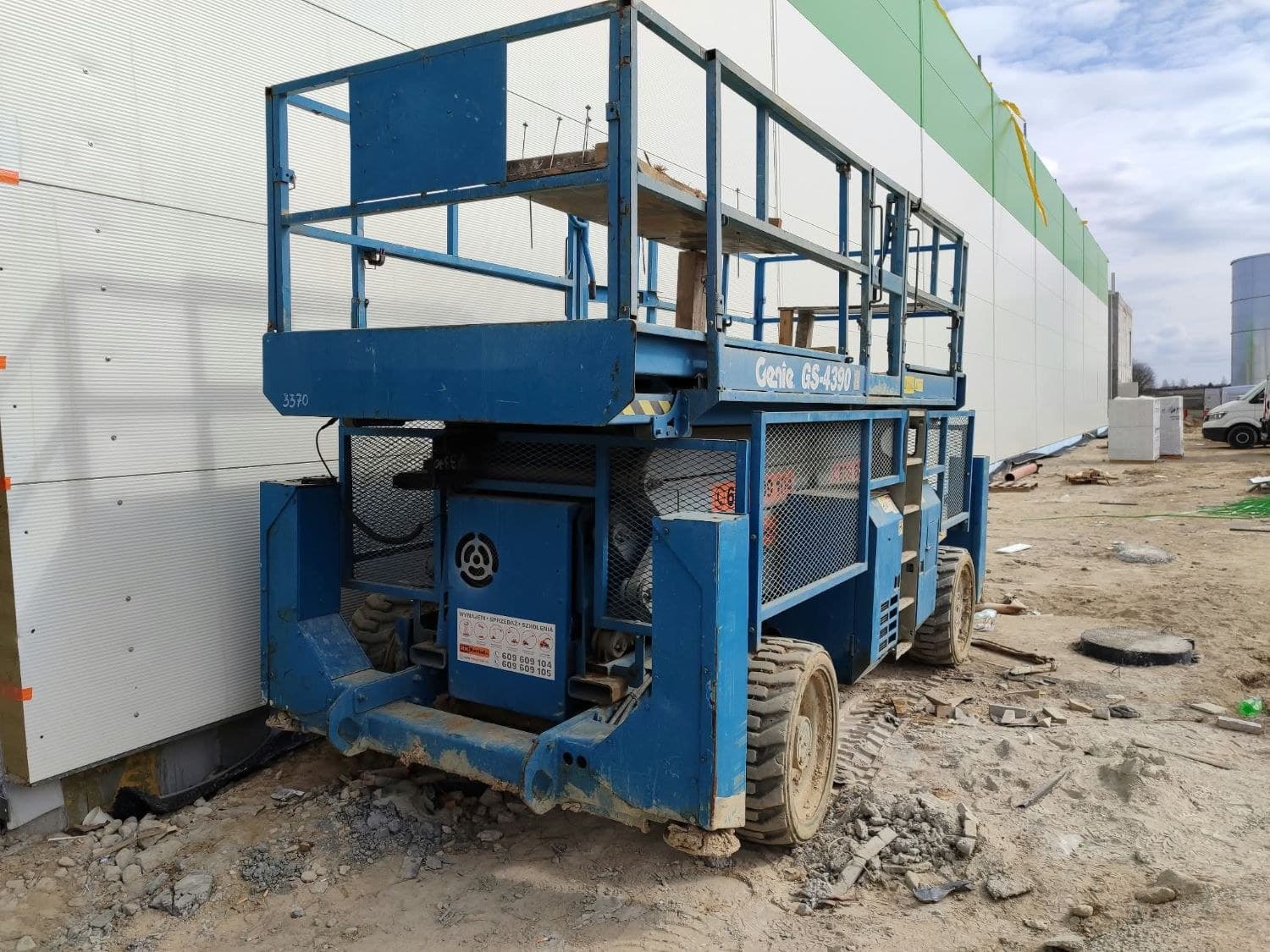Rented Genie GS-4390 RT rough terrain scissor lift (4×4, 15 m, on outriggers) from RK Rental during the installation of sandwich-panel walls on a hall construction site in Szubin