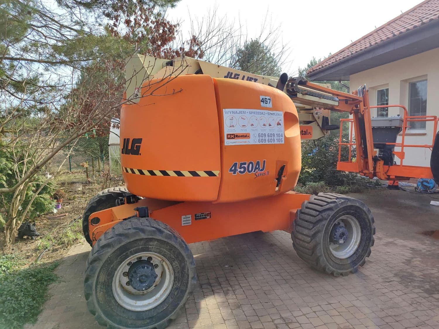 Podnośnik przegubowy JLG 450AJ Series II 4x4 (16 m) RK Rental wynajęty do mycia dachu domu jednorodzinnego