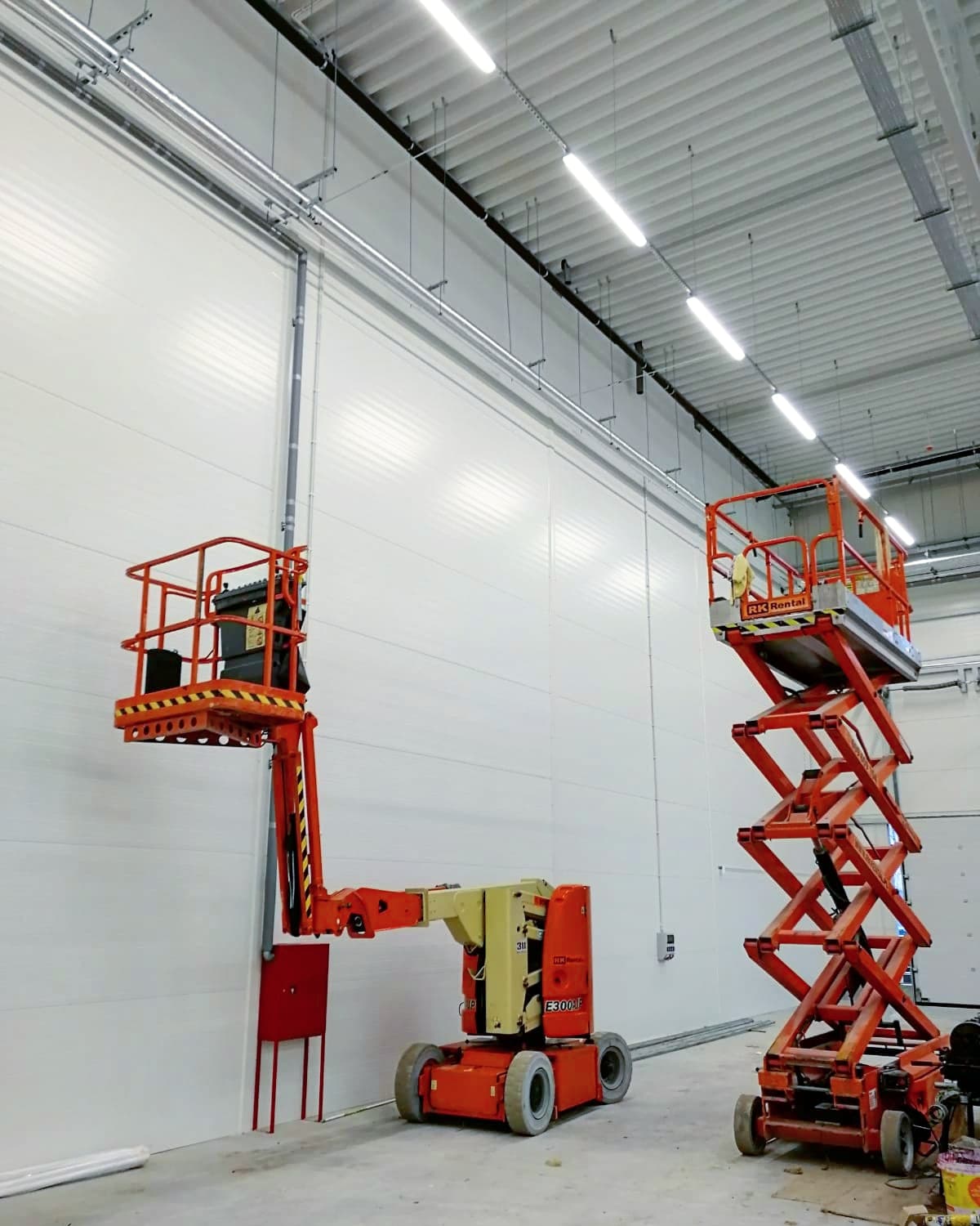 Podnośniki elektryczne JLG E300AJP (przegubowy) i JLG 2030ES (nożycowy) RK Rental podczas prac wewnątrz nowej hali w Poznaniu