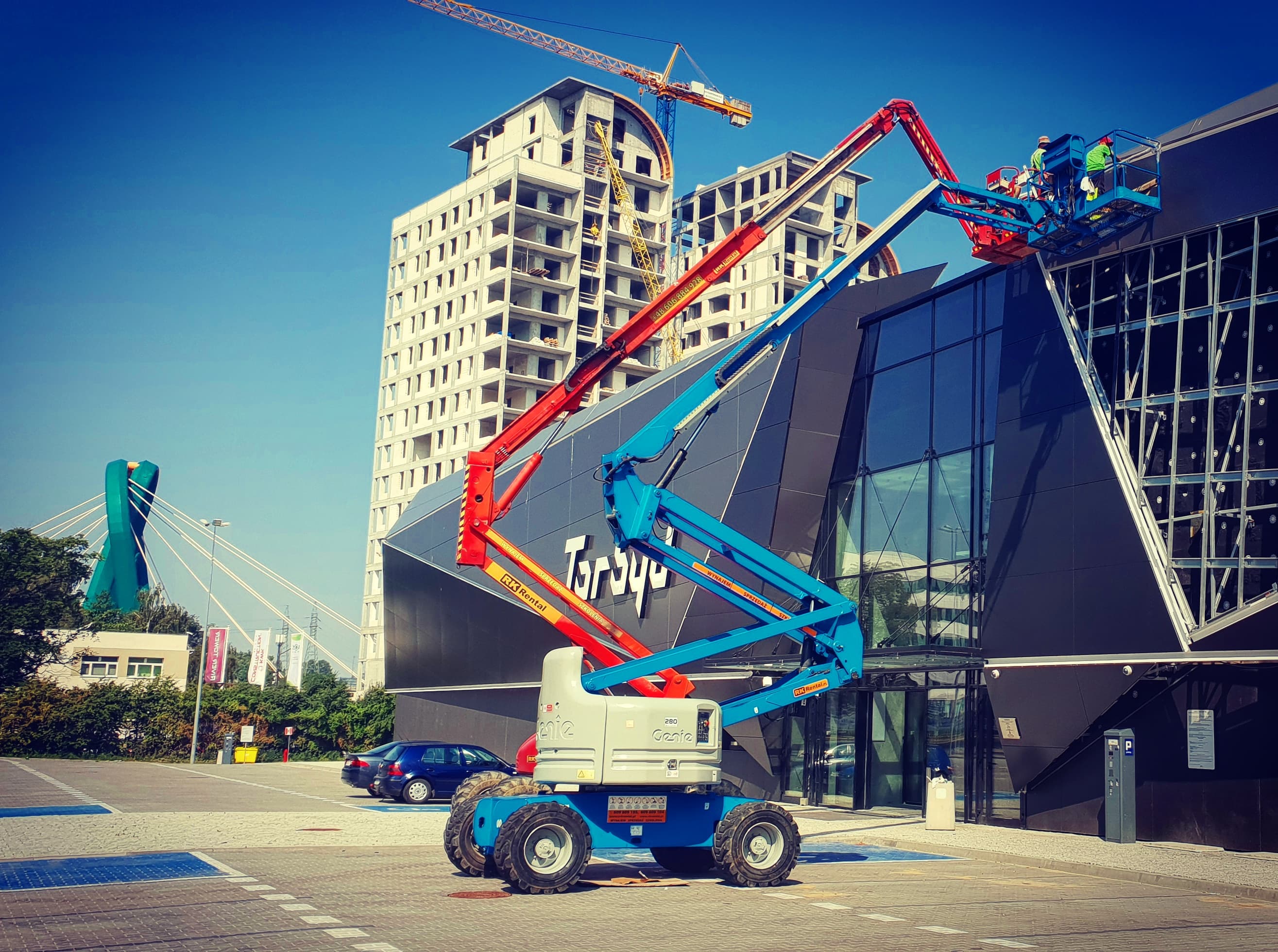 Dwa podnośniki przegubowe Genie Z-60 i Haulotte HA20PX (20 m) RK Rental przy montażu elewacji obiektu sportowego Torbyd w Bydgoszczy